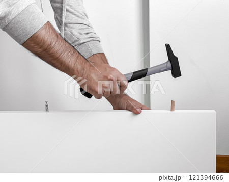 Male adult Caucasian assembling furniture with hammer and wooden pegs 121394666