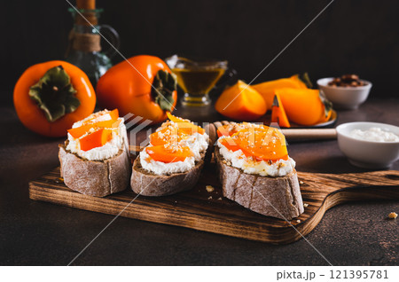 Sandwiches on rye ciabatta with ricotta, persimmon, honey and nuts on a board on a table 121395781
