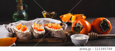 Sandwiches on rye ciabatta with ricotta, persimmon, honey and nuts on a board web banner 121395789