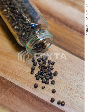 Black Peppercorns Spilled from a Glass Jar on wooden background. High quality photo 121395972
