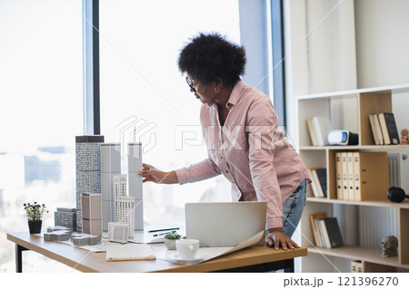 African American female architect in mid 30s developing architectural model for modern urban city in office setting with natural light. 121396270