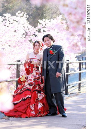 河津桜の咲く風景の中にいる着物風和柄のウエディングドレスを着た新婦様と新郎様 121397055