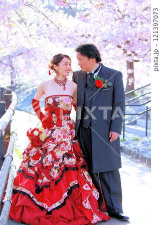 河津桜の咲く風景の中にいる着物風和柄のウエディングドレスを着た新婦様と新郎様 121397073