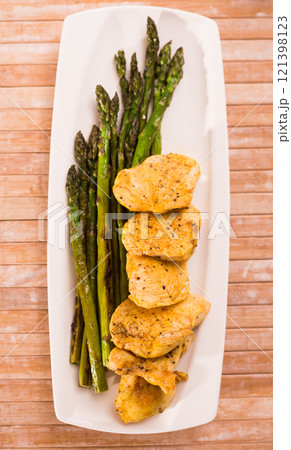 Fried chicken breast pieces with asparagus on white plate. top view 121398123