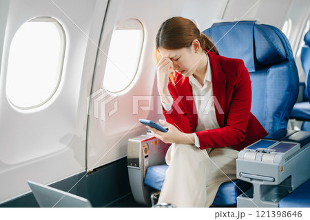 Photo of a frustrated woman sitting on an airplane with her head in her hands. Asian woman sitting 121398646