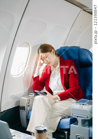 Photo of a frustrated woman sitting on an airplane with her head in her hands. Asian woman sitting 121398647