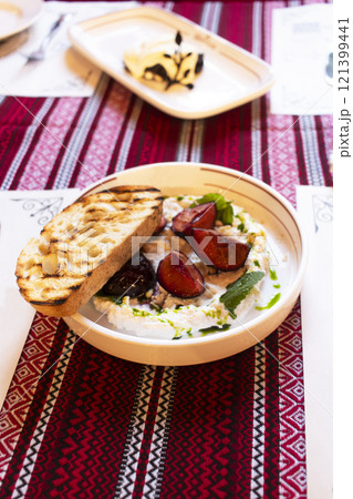 Ricotta cheese spread with sweet plums and a piece of bruchetta on a white plate 121399441