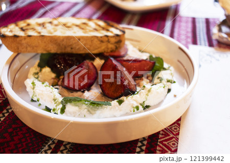 Ricotta cheese spread with sweet plums and a piece of bruchetta on a white plate Ricotta cheese spread with sweet plums and a piece of bruchetta on a white plate 121399442