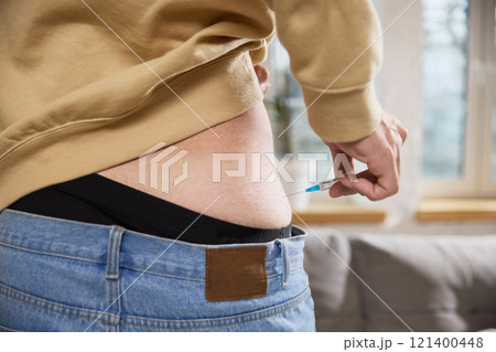 Close-up of sick man administering injection into his lower back with syringe. Treatment at home and disease. 121400448