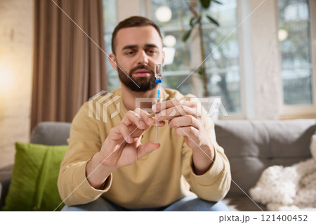 Focused man draws solution for injection into syringe preparing to injecting treatment at home. Focused man draws solution for injection into syringe preparing to injecting treatment at home. 121400452