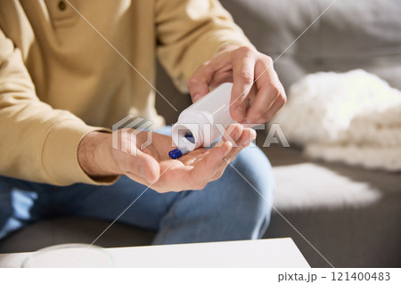 Cropped photo of male hands pours tablets, vitamins or dietary supplements into hand at desk. Strengthening immune system. 121400483