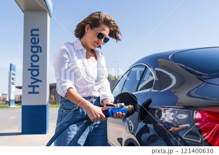 Woman holds a hydrogen fueling nozzle on a hydrogen filling station. Refueling car with hydrogen fuel. Woman holds a hydrogen fueling nozzle on a hydrogen filling station. Refueling car with hydrogen fuel. 121400630