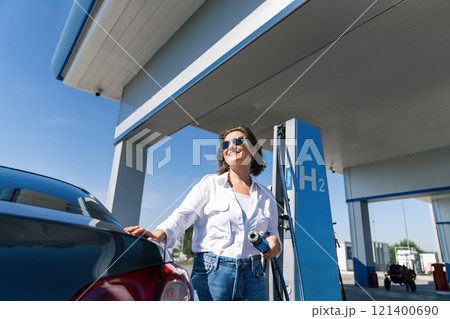 Woman holds a hydrogen fueling nozzle on a hydrogen filling station. Refueling car with hydrogen fuel Woman holds a hydrogen fueling nozzle on a hydrogen filling station. Refueling car with hydrogen fuel 121400690