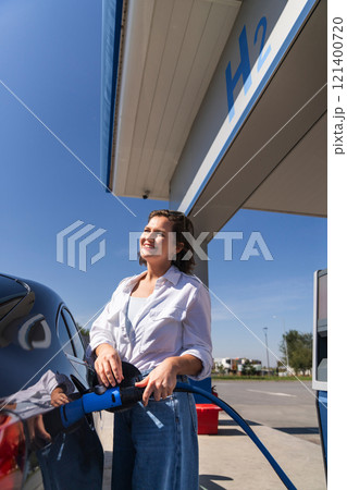 Woman holds a hydrogen fueling nozzle on a hydrogen filling station. Refueling car with hydrogen fuel 121400720