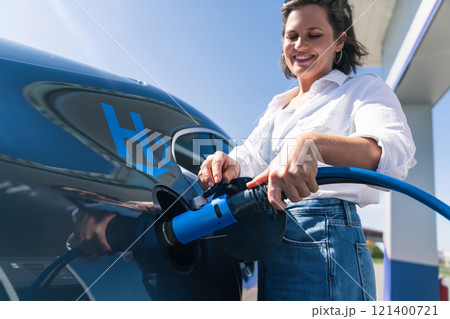 Woman holds a hydrogen fueling nozzle on a hydrogen filling station. Refueling car with hydrogen fuel Woman holds a hydrogen fueling nozzle on a hydrogen filling station. Refueling car with hydrogen fuel 121400721