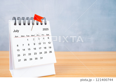 July 2025 calendar and red push pin on table. 121400744
