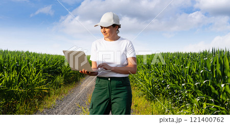 Woman farmer wearing white cap and t-shirt with laptop on agricultural field 121400762