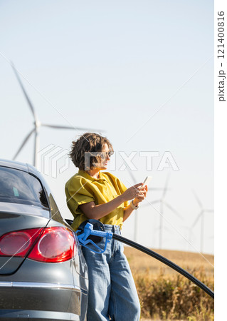 Woman with fueling hydrogen car. Refueling car with hydrogen fuel. Wind turbines in the background Woman with fueling hydrogen car. Refueling car with hydrogen fuel. Wind turbines in the background 121400816