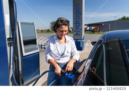 Woman holds a hydrogen fueling nozzle on a hydrogen filling station. Refueling car with hydrogen fuel. Woman holds a hydrogen fueling nozzle on a hydrogen filling station. Refueling car with hydrogen fuel. 121400829