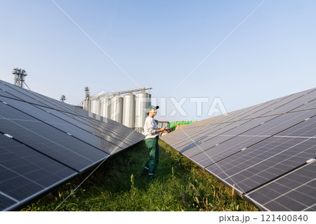 Female farmer with digital tablet on a modern farm using solar panels. Agricultural silos in the background. 121400840
