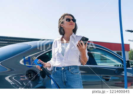 Woman holds a hydrogen fueling nozzle on a hydrogen filling station. Refueling car with hydrogen fuel 121400845