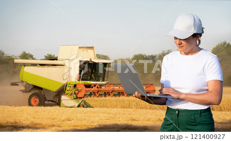 Female farmer with laptop on a background of harvester. Smart farming concept. Female farmer with laptop on a background of harvester. Smart farming concept. 121400927