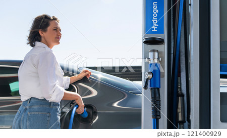 Woman holds a hydrogen fueling nozzle on a hydrogen filling station. Refueling car with hydrogen fuel Woman holds a hydrogen fueling nozzle on a hydrogen filling station. Refueling car with hydrogen fuel 121400929