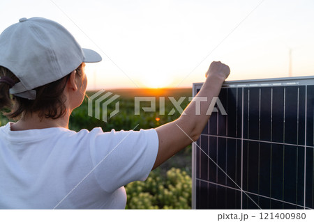 Woman wearing white cap stands next to solar panel at sunset Woman wearing white cap stands next to solar panel at sunset 121400980