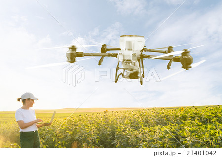 Woman farmer controls drone sprayer with a laptop. Smart farming and precision agriculture 121401042