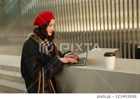 A Stylish Young Woman is Working Diligently on Her Laptop in a Vibrant Urban Setting A Stylish Young Woman is Working Diligently on Her Laptop in a Vibrant Urban Setting 121401698
