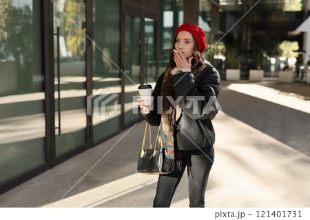 A Stylish Woman is Enjoying Her Coffee Outdoors in a Vibrant Urban Setting Today 121401731