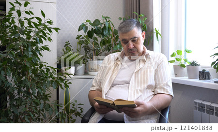 Man Reading Book in Armchair Surrounded by Indoor Plants Man Reading Book in Armchair Surrounded by Indoor Plants 121401838