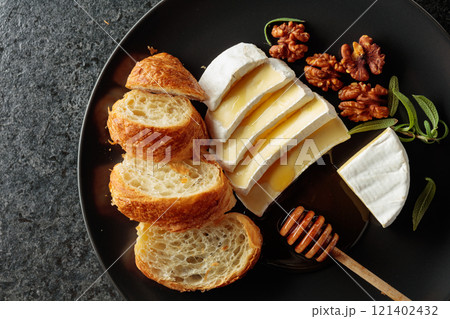 Camembert cream cheese with honey, croissants, and walnuts on a black plate. 121402432