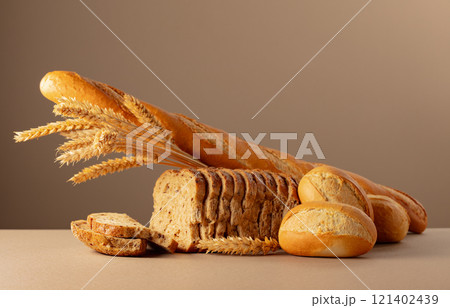 Sliced bread, baguette, and French buns with wheat ears on a beige background. 121402439