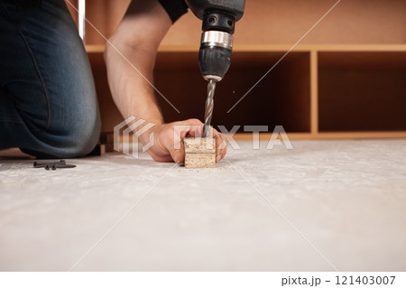 A man drills a hole in the wood against the background of an inverted closet on the floor. 121403007