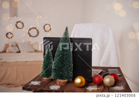New Year's interior, decoration of the desktop and bedroom for Christmas. Boke, lights, Christmas trees, balloons, a table with a laptop with decorations. White room, wooden furniture. 121403008