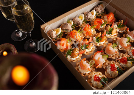 Champagne, tartlets, seafood salads. Cardboard box with food with home delivery. Gift for holiday, party, family dinner. Catering. Delicious snacks. 121403064