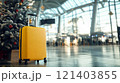 Yellow suitcase standing near christmas tree in airport terminal symbolizing christmas vacation 121403855