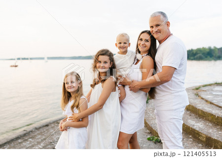 Happy family of five, including couple and three children are posing for a photo on pier by the water 121405513