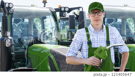 Man with biofuel refueling nozzle next to agricultural machines 121405647