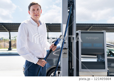 Man holds a hydrogen fueling nozzle on a hydrogen filling station. Refueling car with hydrogen fuel 121405664