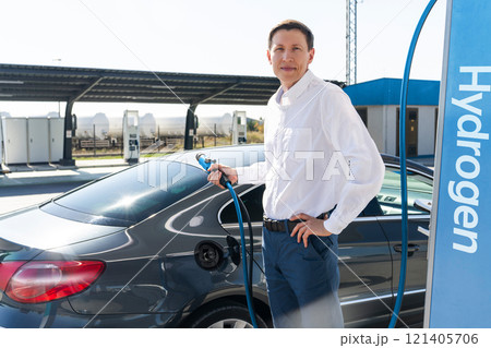 Man holds a hydrogen fueling nozzle on a hydrogen filling station. Refueling car with hydrogen fuel Man holds a hydrogen fueling nozzle on a hydrogen filling station. Refueling car with hydrogen fuel 121405706