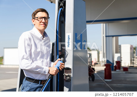 Man holds a hydrogen fueling nozzle on a hydrogen filling station. Refueling car with hydrogen fuel. Man holds a hydrogen fueling nozzle on a hydrogen filling station. Refueling car with hydrogen fuel. 121405707