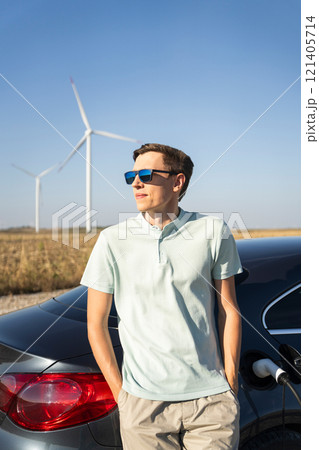 Man with charging electric car. Wind turbines in the background 121405714