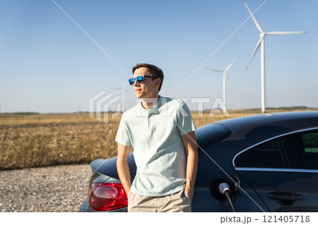 Man with charging electric car. Wind turbines in the background Man with charging electric car. Wind turbines in the background 121405718