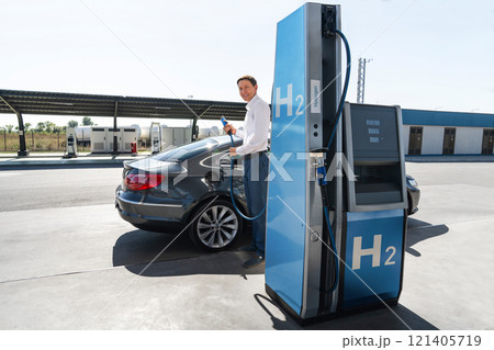 Man holds a hydrogen fueling nozzle on a hydrogen filling station. Refueling car with hydrogen fuel. Man holds a hydrogen fueling nozzle on a hydrogen filling station. Refueling car with hydrogen fuel. 121405719
