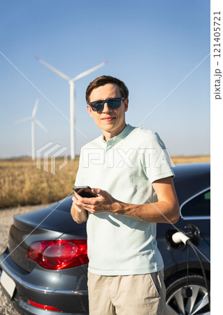 Man with charging electric car. Wind turbines in the background Man with charging electric car. Wind turbines in the background 121405721