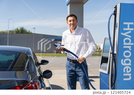 Man holds a hydrogen fueling nozzle on a hydrogen filling station. Refueling car with hydrogen fuel Man holds a hydrogen fueling nozzle on a hydrogen filling station. Refueling car with hydrogen fuel 121405724