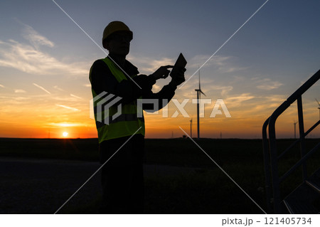 Engineer with digital tablet works on a field of wind turbines at sunset. Engineer with digital tablet works on a field of wind turbines at sunset. 121405734