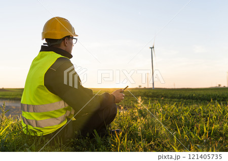 Worker sits on the grass and looks at wind turbines Worker sits on the grass and looks at wind turbines 121405735